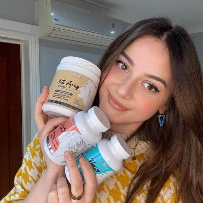 Woman holding three supplement containers in a room with an air conditioner.