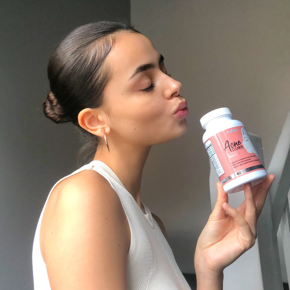 Woman holding a supplement bottle labeled Acne cleanse against a neutral background